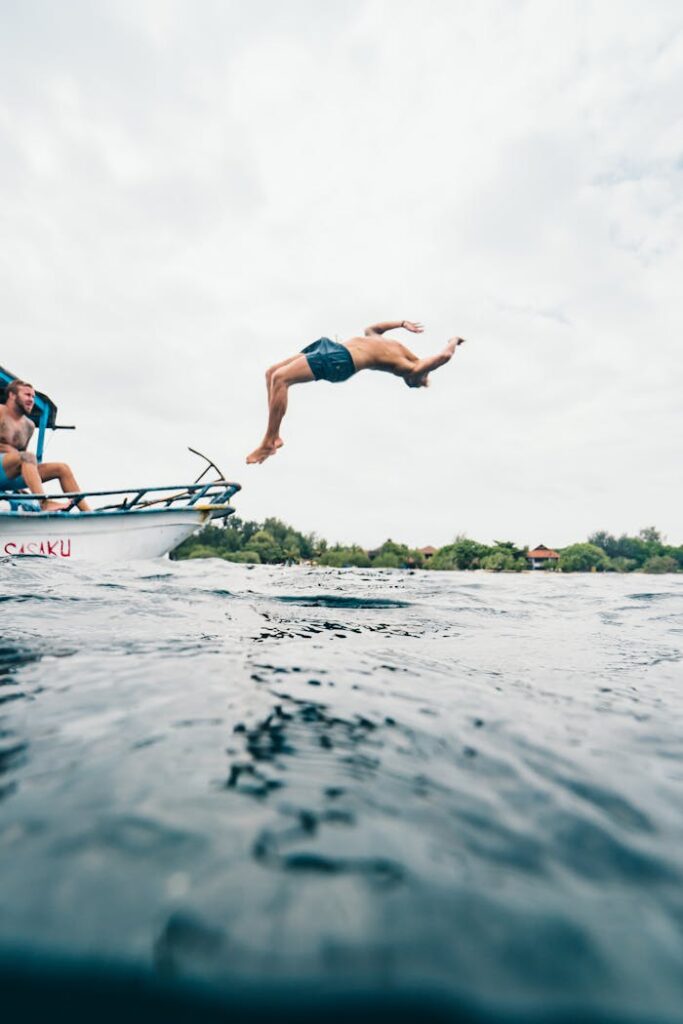 A man performs a backflip dive into the ocean from a boat, capturing a moment of adventure in Indonesia.