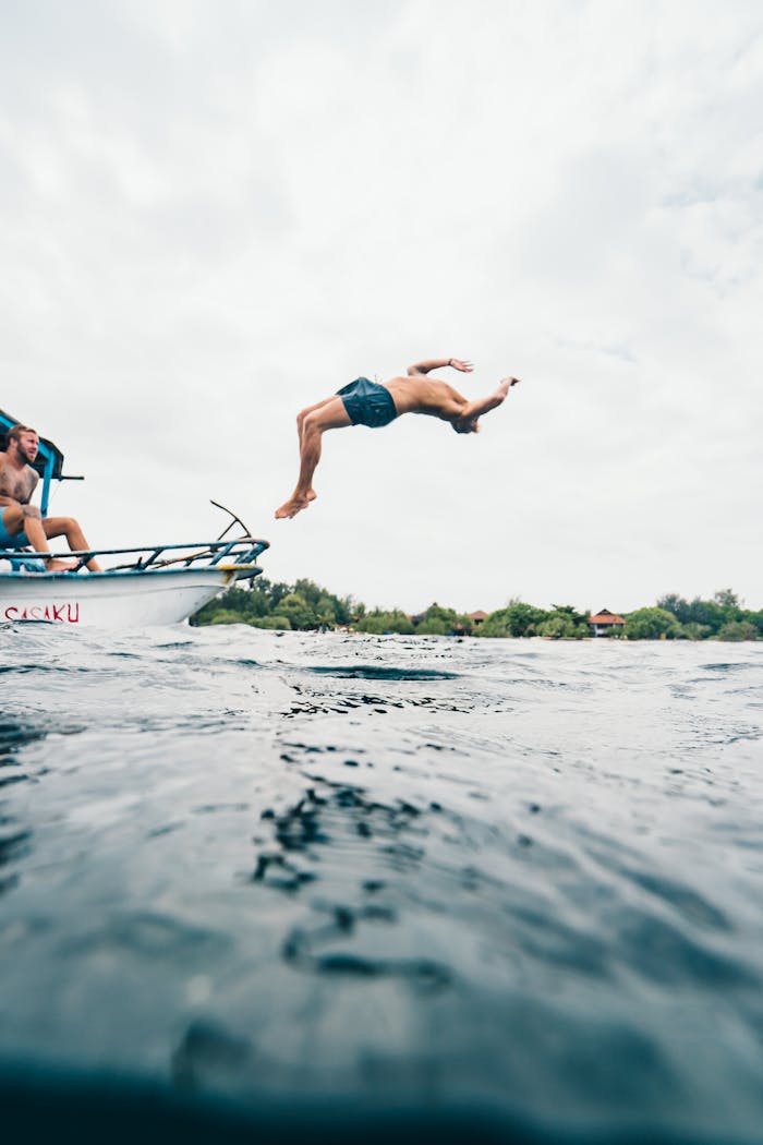 A man performs a backflip dive into the ocean from a boat, capturing a moment of adventure in Indonesia.