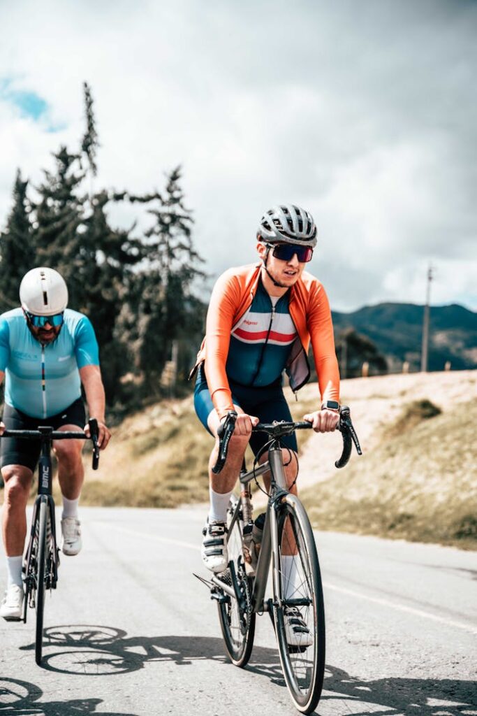 Two cyclists in sportswear ride road bikes outdoors on a sunny day with scenic background.