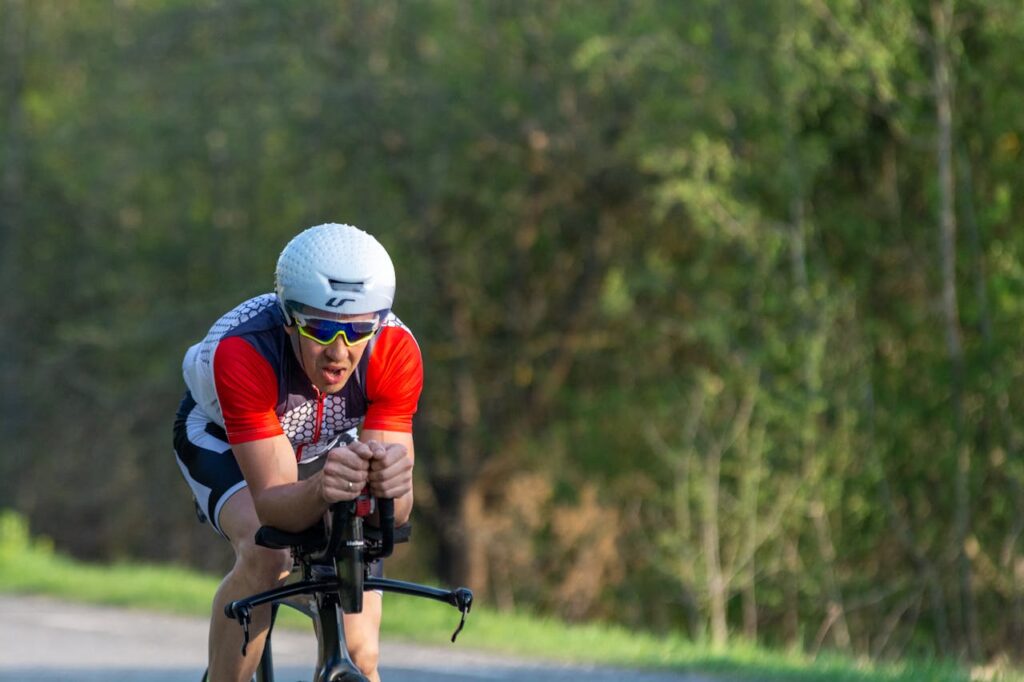 Triathlete cycling fast on a rural road during training, wearing a helmet and sunglasses.